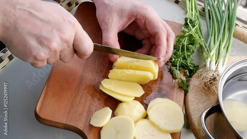 Top view of male hands cutting potato slices on wooden board