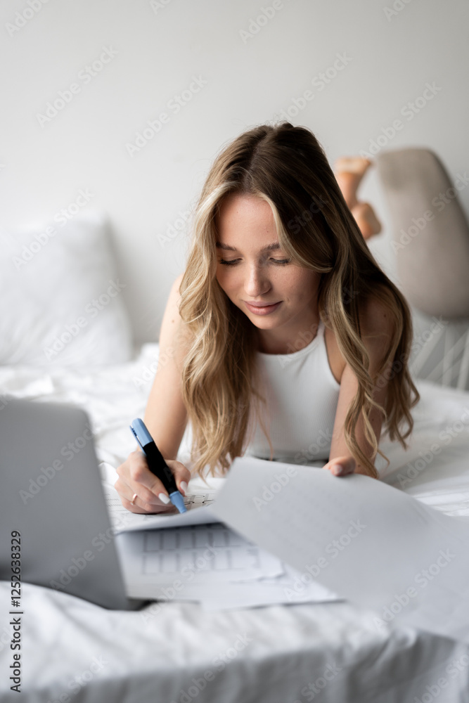 woman using laptop computer working with paper documents laying on bed in bedroom. Indoor leisure activity. woman using laptop computer working with paper documents laying on bed in bedroom. Indoor leisure activity.