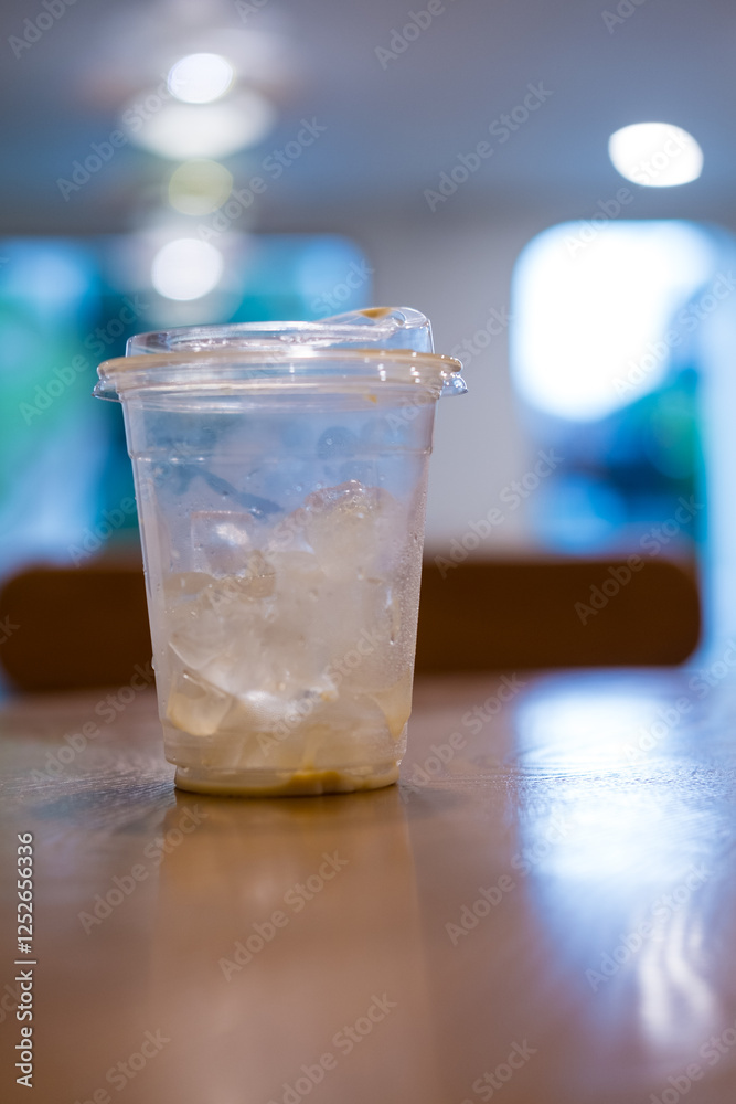 Close up of iced coffee plastic cup with a little ice on wood desk blurred background Close up of iced coffee plastic cup with a little ice on wood desk blurred background