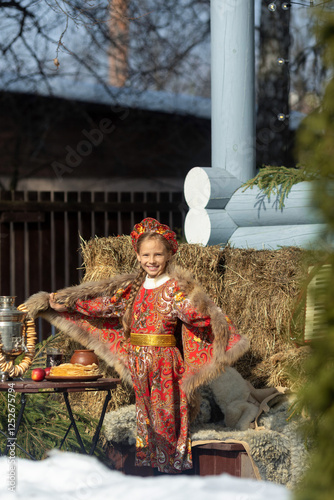 A blonde girl in a national Russian costume on the Maslenitsa holiday. A beautiful russian girl in a national costume made of a fur cape and kokoshnik on the background of a hayloft. 