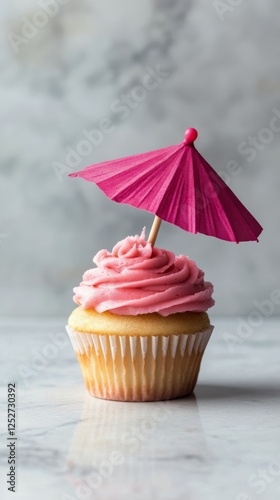 Pink frosted cupcake with a mini umbrella decoration in a bright setting