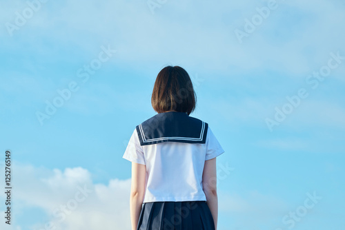 青空と海を背景に立つ女子高校生
