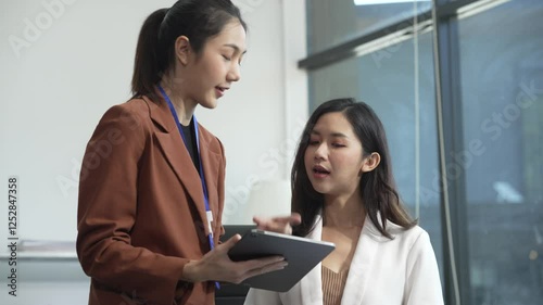 Two Asian female business woman sit desk,discussing business investments.They analyze financial data, explore market opportunities, and strategic growth to maximize returns ensure business success