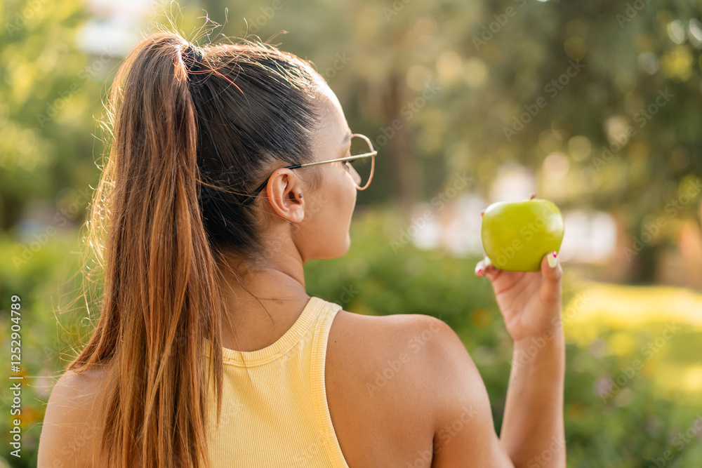 Young pretty woman with an apple at outdoors in back position Young pretty woman with an apple at outdoors in back position