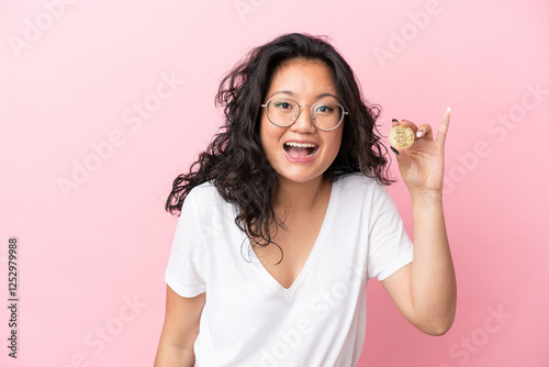 Young asian woman holding a Bitcoin isolated on pink background with surprise facial expression photo