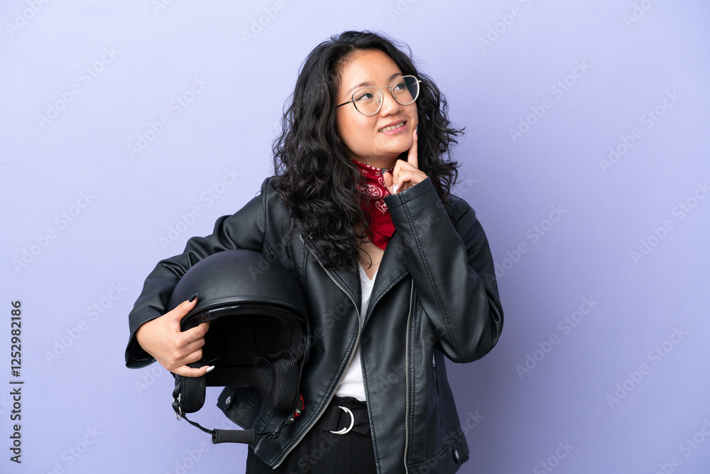 Young asian woman with a motorcycle helmet isolated on purple background thinking an idea while looking up Young asian woman with a motorcycle helmet isolated on purple background thinking an idea while looking up