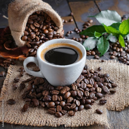 White coffee cup standing on roasted coffee beans with burlap sack