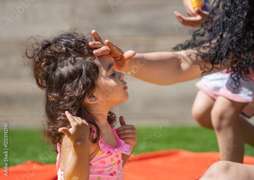 Mother applying sunscreen lotion to her daughter's forehead on a sunny summer day