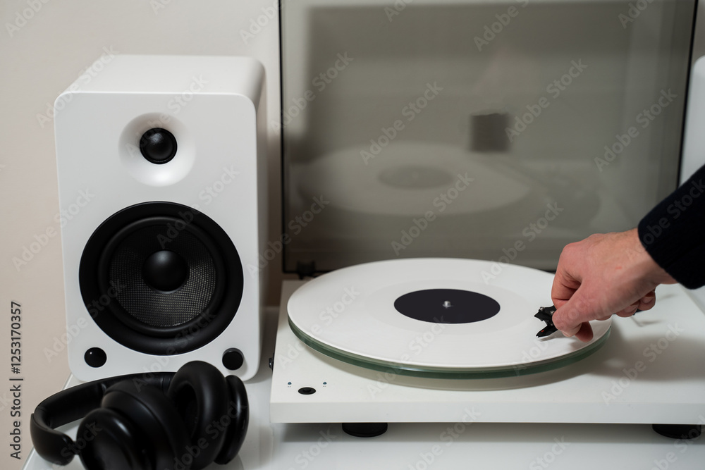 Fototapeta premium Musician places a white vinyl record into a turntable to enjoy soundtracks with Hi-Fi and LP. White vinyl player with speaker system and rock record in white shade.