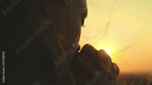 girl prays looking sunset, long hair flying away in glare sunlight rays strong wind, looking at dawn, lonely hike of brave girl, looking into sky with her eyes, believing good. close-up hands face