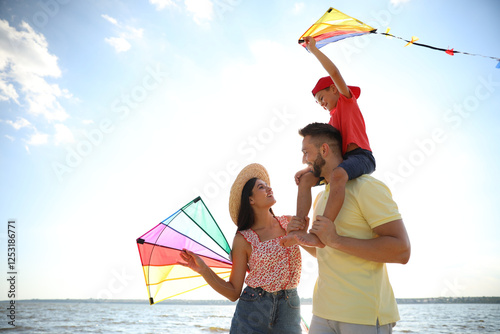 Happy parents and their child playing with kites near sea. Spending time in nature