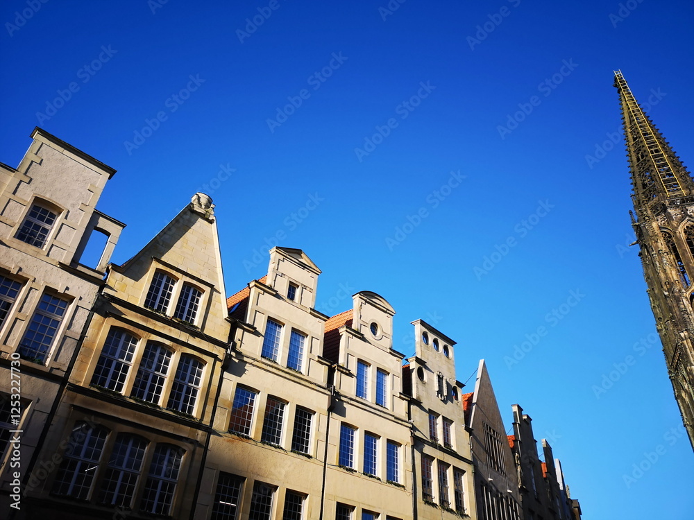 Fototapeta premium Schöne alte Giebelhäuser vor blauem Himmel bei Sonnenschein am Prinzipalmarkt mit dem Kirchturm der römisch-katholischen Kirche St. Lamberti in der Altstadt von Münster in Westfalen im Münsterland