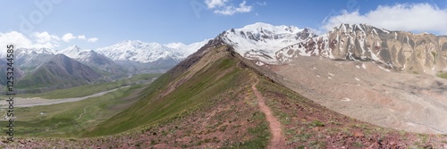 Wide panoramic view on centered ridgeline dividing green valley from snowy peaks of Pamir Mountains photo