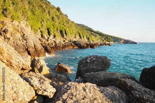 Waves gently crash against the rugged rocks while the sun sets over the horizon. Experience the serene beauty of this coastal location filled with natural wonders. Canj, Montenegro, Adriatic sea photo