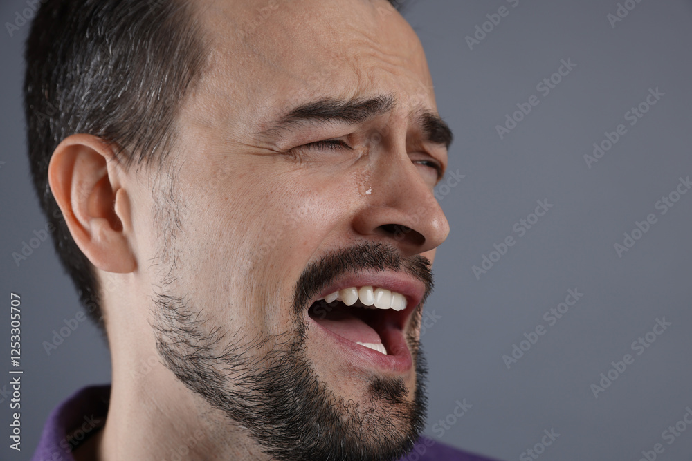 Fototapeta premium Sad man crying on grey background, closeup. Space for text