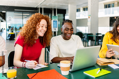 Diverse group of college students studying together at university cafeteria. Happy classmate friends talking while preparing exam or doing group work sitting on bar table outside. Education concept.