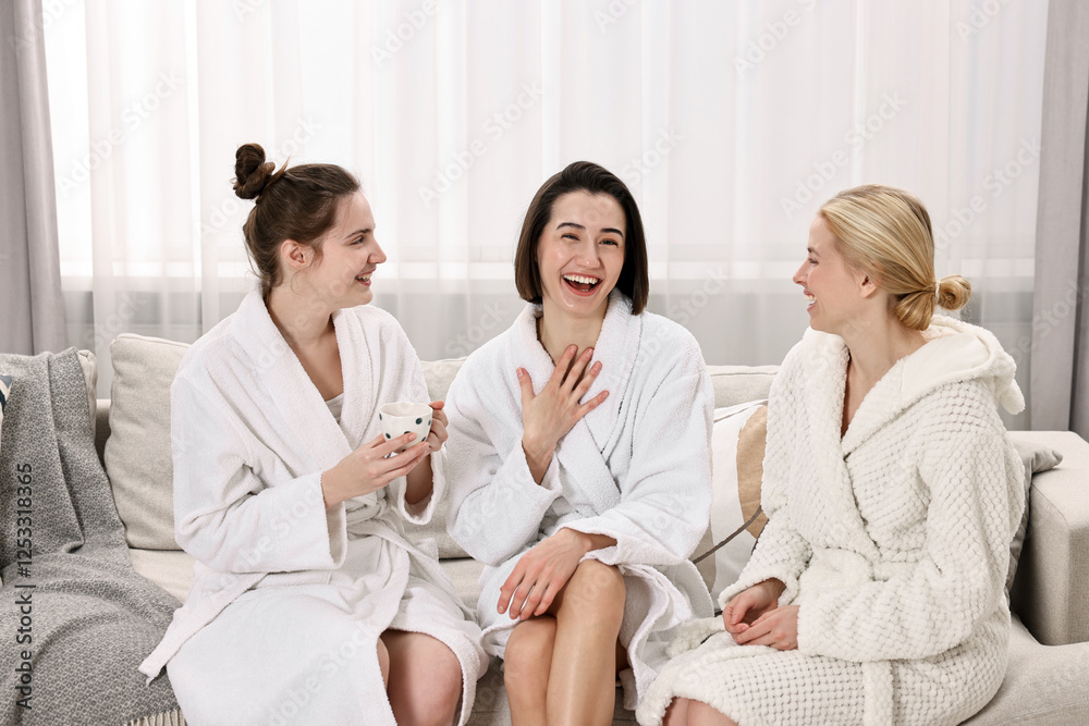 Fototapeta premium Cheerful women in bathrobes resting on sofa at spa