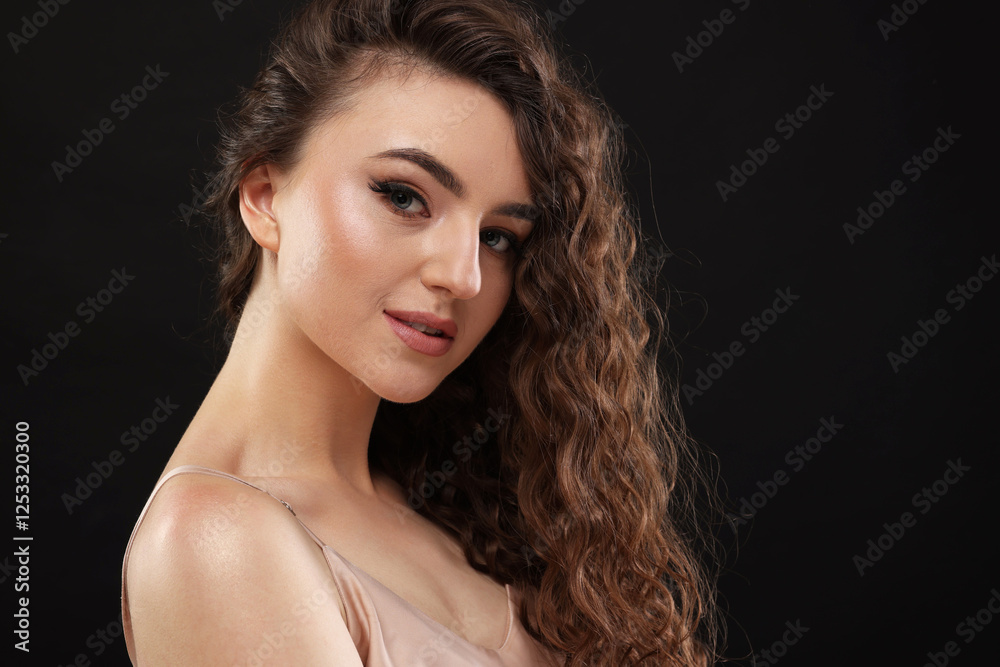 Fototapeta premium Beautiful young woman with long curly brown hair on black background, space for text