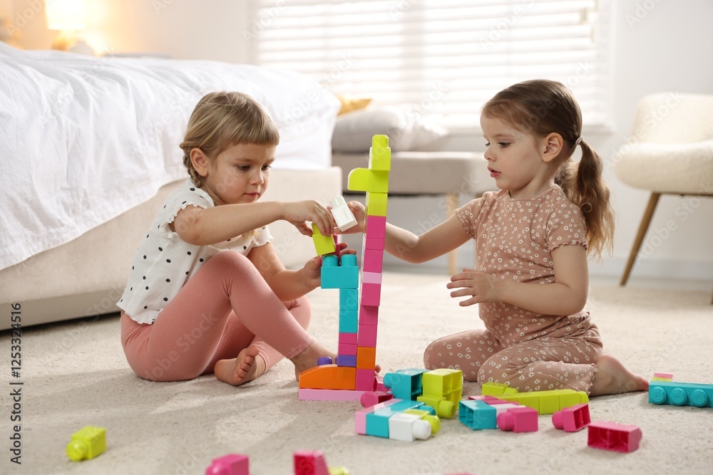 Cute little sisters playing with colorful building blocks on floor at home Cute little sisters playing with colorful building blocks on floor at home