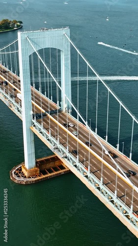 Cars going to and from the Bronx, New York. Aerial view of the Throgs Neck Bridge on sunny day. Boats sailing on the East River at backdrop. Vertical video photo