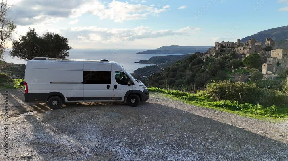 Aerial view of a large camper van parked near historic stone buildings and scenic hills, Vathia, Greece. Aerial view of a large camper van parked near historic stone buildings and scenic hills, Vathia, Greece.