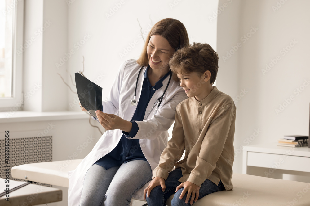 Obraz premium Useful radiation. Caring attentive young female nurse doctor pediatrician surgeon radiologist make x ray diagnostics study radiograph together with interested young patient boy describe picture to kid