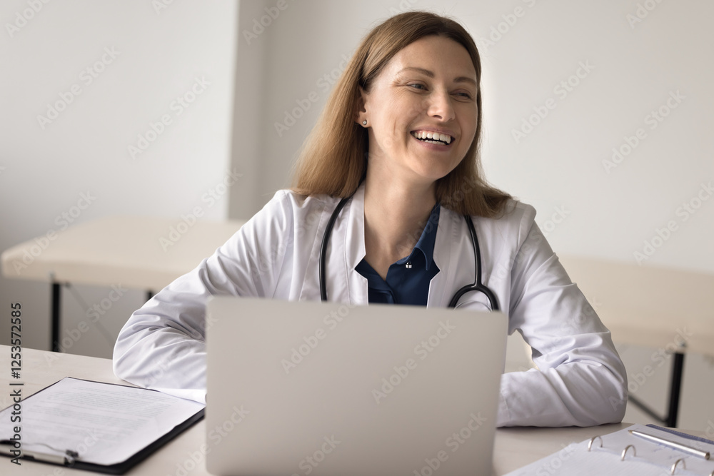 Joyful smiling millennial female doctor in white coat uniform general practitioner medical laboratory worker pharmacist sit by notebook computer laughing having fun enjoy profession feel happy at work Joyful smiling millennial female doctor in white coat uniform general practitioner medical laboratory worker pharmacist sit by notebook computer laughing having fun enjoy profession feel happy at work