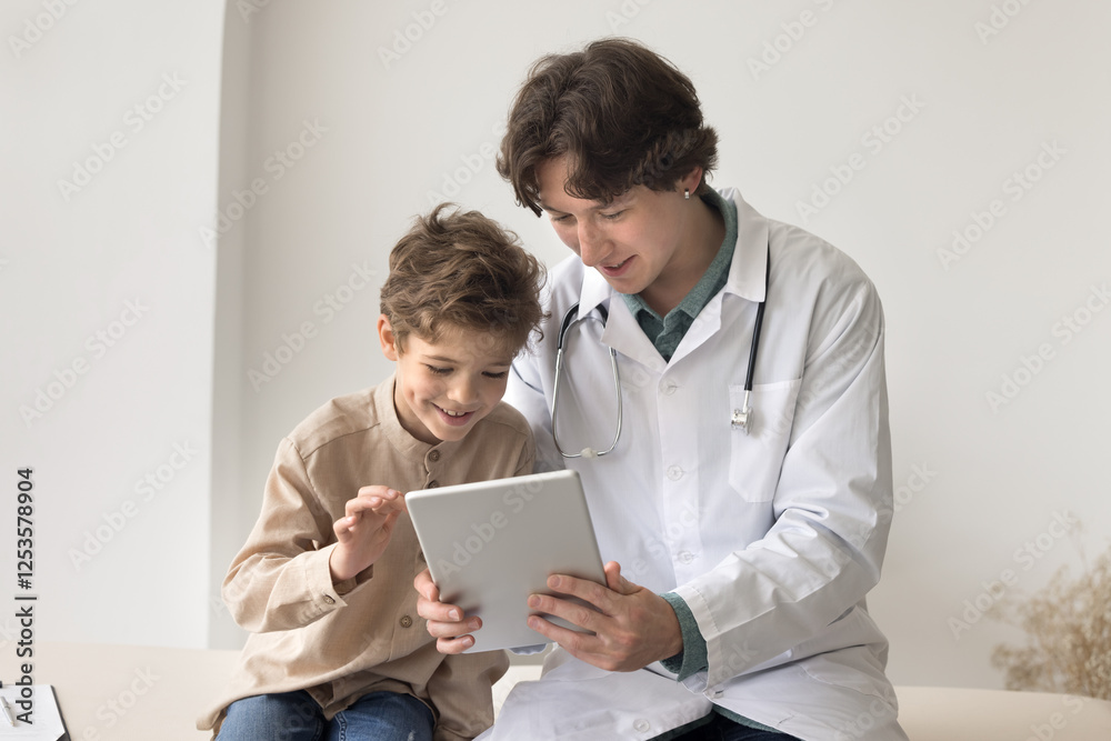 Caring young male doctor surgeon pediatrician use tablet pc on meeting with little boy play video game with child to relieve patient stress before medical procedure examination make contact with kid Caring young male doctor surgeon pediatrician use tablet pc on meeting with little boy play video game with child to relieve patient stress before medical procedure examination make contact with kid
