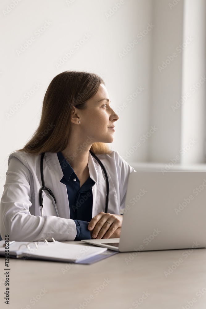 Vertical portrait confident young woman doctor sit at clinic office desk work with papers after seeing patients look away rest distracted from notebook screen think of career in healthcare plan report Vertical portrait confident young woman doctor sit at clinic office desk work with papers after seeing patients look away rest distracted from notebook screen think of career in healthcare plan report