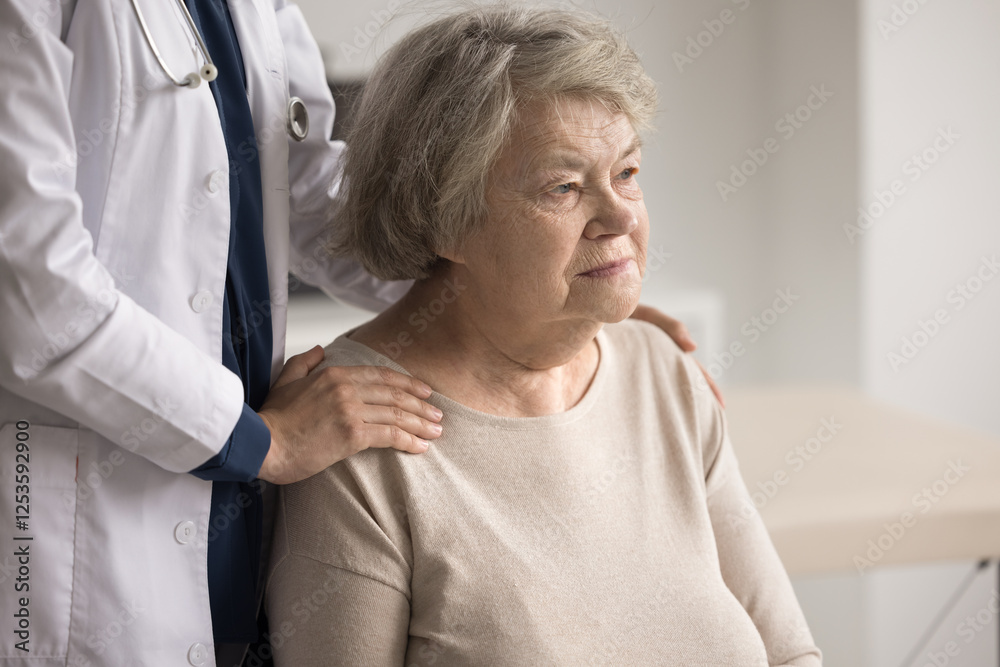 Fototapeta premium Older female retiree patient of nursing home for elderly people sit on chair look away feel support of caregiver nurse hugging her shoulders from back. Medical aid for aged persons concept. Copy space