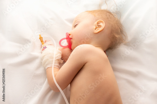 Obraz na płótnie Babygirl sick and sleeping on patient bed at the hospital. Saline intravenous or (IV)drip in baby patient hand. Poor baby looks tired and exhausted.IV fluid replacement or correcting the dehydration w salonie