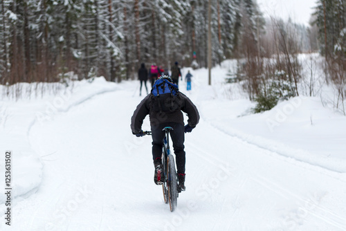A man rides a bicycle through the snow in the park in winter.