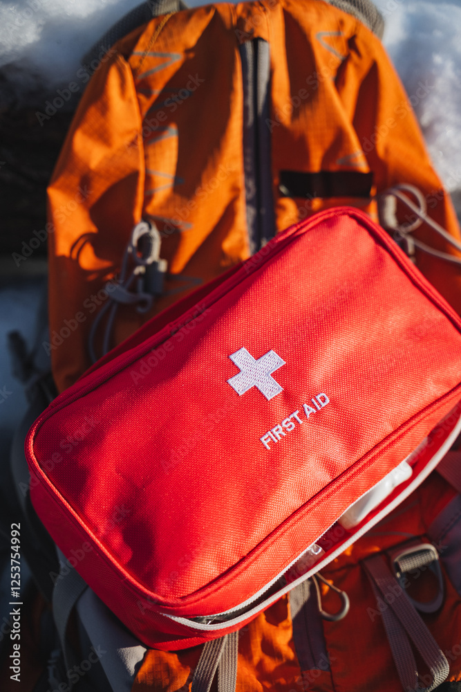 Naklejka premium A bright red first aid bag is resting comfortably atop an orange backpack, which serves as a practical solution for carrying personal belongings during travel or outdoor excursions