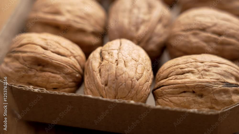 Whole walnuts in cardboard box on wooden surface. Natural nut snack packed in eco-friendly packaging. Macro. Rotation Whole walnuts in cardboard box on wooden surface. Natural nut snack packed in eco-friendly packaging. Macro. Rotation