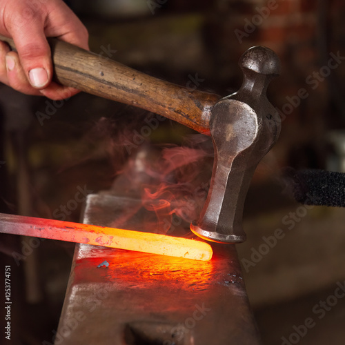 A shaped hammer being used to strike and shape hot metal on an anvil in a blacksmiths forge