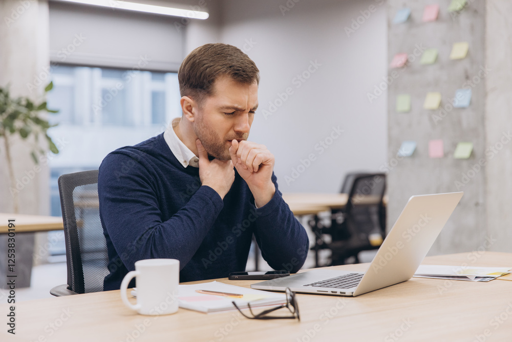 Businessman coughing while working at his desk in the office, suffering from seasonal flu or allergies Businessman coughing while working at his desk in the office, suffering from seasonal flu or allergies