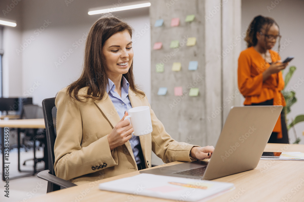 Diverse team collaborating in contemporary workplace, woman typing on laptop, colleague reviewing smartphone nearby, corporate setting Diverse team collaborating in contemporary workplace, woman typing on laptop, colleague reviewing smartphone nearby, corporate setting