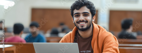 An Indian student sitting in the classroom and smiling while using their laptop
