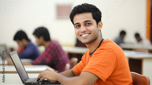 An Indian student sitting in the classroom and smiling while using their laptop
