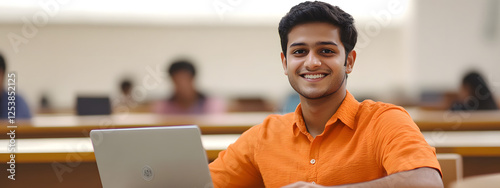 An Indian student sitting in the classroom and smiling while using their laptop
