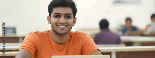 An Indian student sitting in the classroom and smiling while using their laptop
