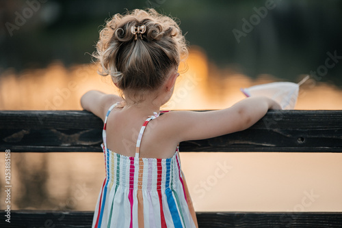 Canvas Print A small girl about 5 years old standing with her back to the camera, looking at a warm sunset horizon