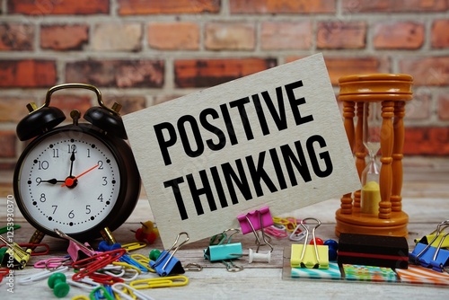 Positive Thinking text on paper card with alarm clock and stationary on wooden background photo