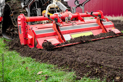 A mini tractor with a milling attachment plows the land in an agricultural field, the milling cutter is close-up
