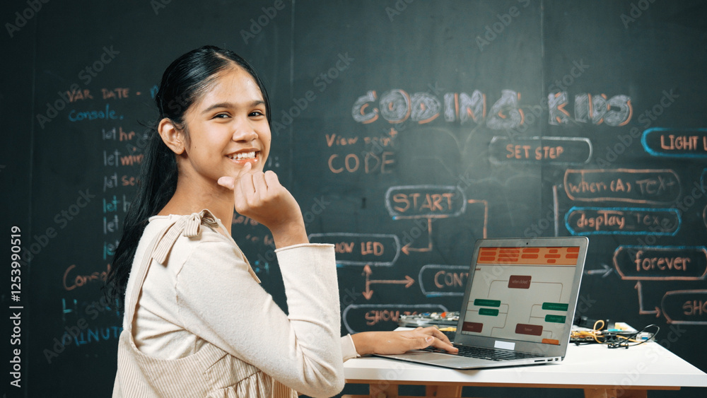 Smart girl using laptop coding or programing system at blackboard. Happy highschool student working on laptop while showing miniheart and looking at camera at STEM technology class. Edification. Smart girl using laptop coding or programing system at blackboard. Happy highschool student working on laptop while showing miniheart and looking at camera at STEM technology class. Edification.