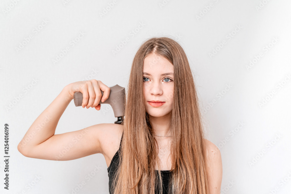 A young woman massages her back and shoulders with percussion massage herself. A young woman massages her back and shoulders with percussion massage herself.
