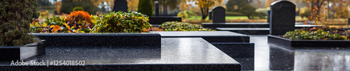 Polished granite tombstones in a cemetery after rain. Reflections on wet surfaces create a serene and peaceful atmosphere in an autumn setting.