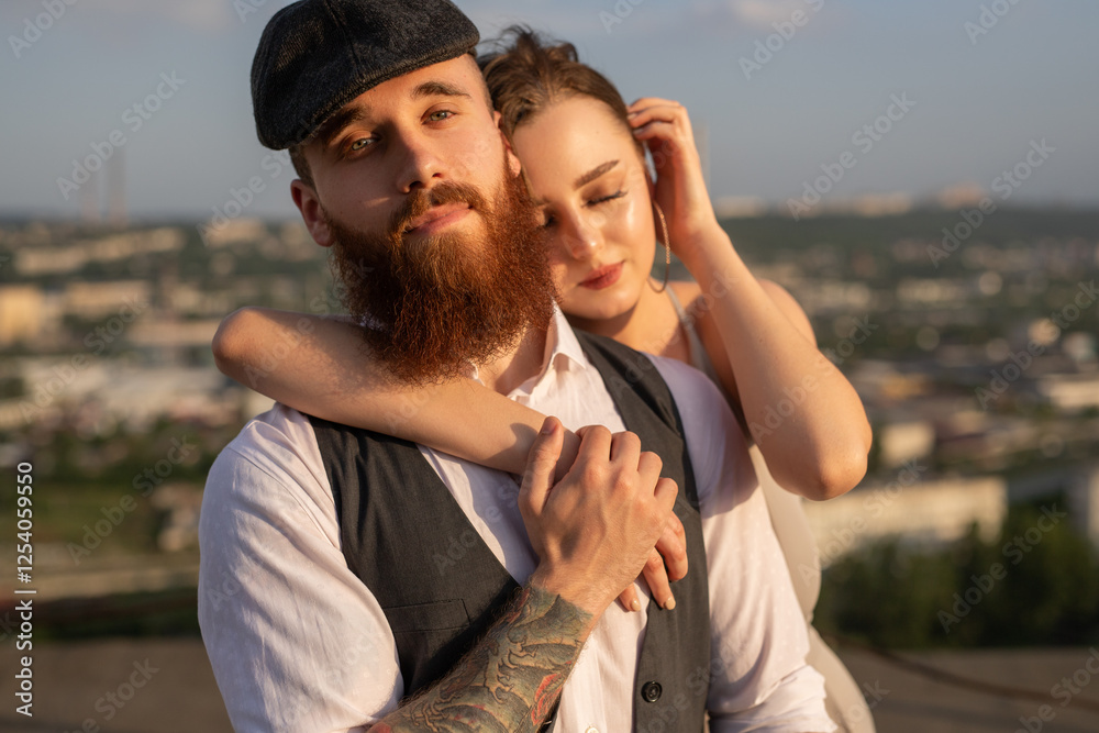 Fototapeta premium A young couple shares a romantic moment on a rooftop during sunset, embracing tenderly. The cityscape in the background adds depth, while the warm evening light highlights their affection and