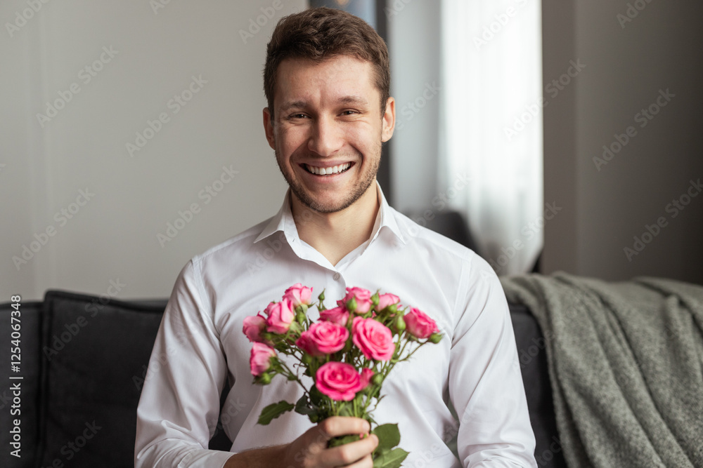 A cheerful man wearing a white shirt sits on a couch, holding a bouquet of pink roses, symbolizing love and happiness, perfect for Valentine's Day or romantic concepts. A cheerful man wearing a white shirt sits on a couch, holding a bouquet of pink roses, symbolizing love and happiness, perfect for Valentine's Day or romantic concepts.
