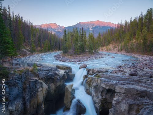 High mountains during sunrise. Waterfall among rocks and forest. Rocky Mounta...